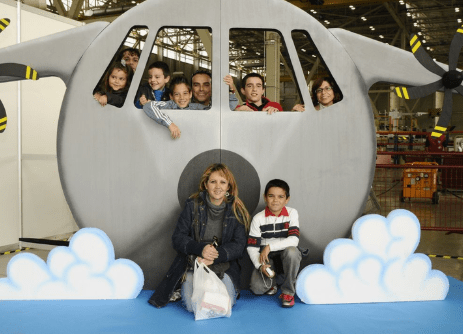 Grupo de personas posando en una escenografía de avión con nubes, como parte de una actividad lúdica en evento corporativo o familiar.